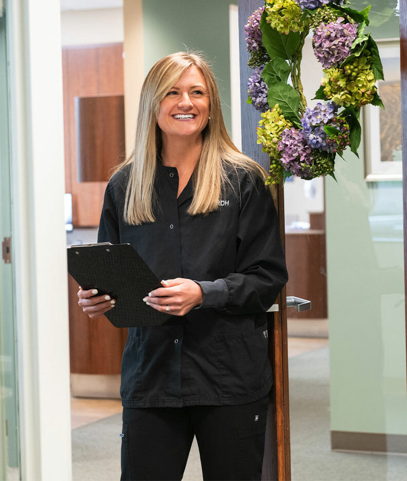 Dental hygienist with clipboard smiling besides a wreath