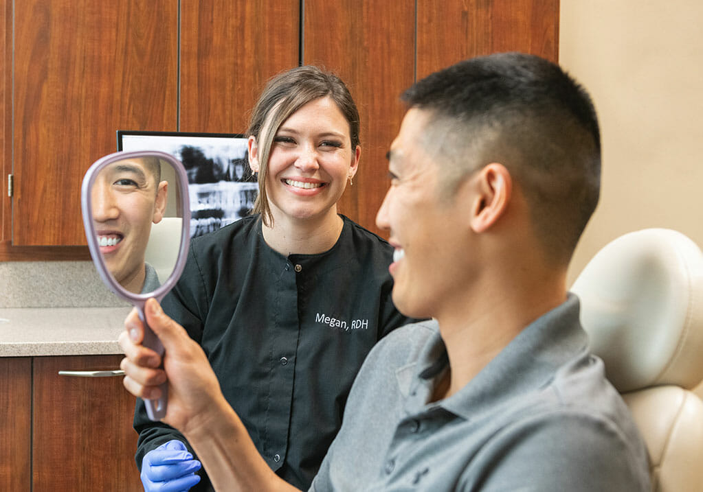 Dental hygienist watching patient smile at his reflection in mirror