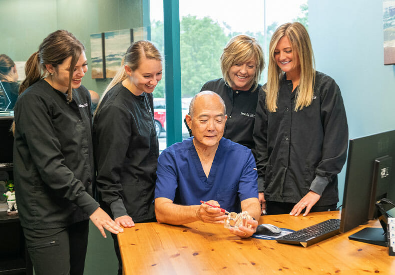 Dr. Sato working on model of teeth while his dental team watches